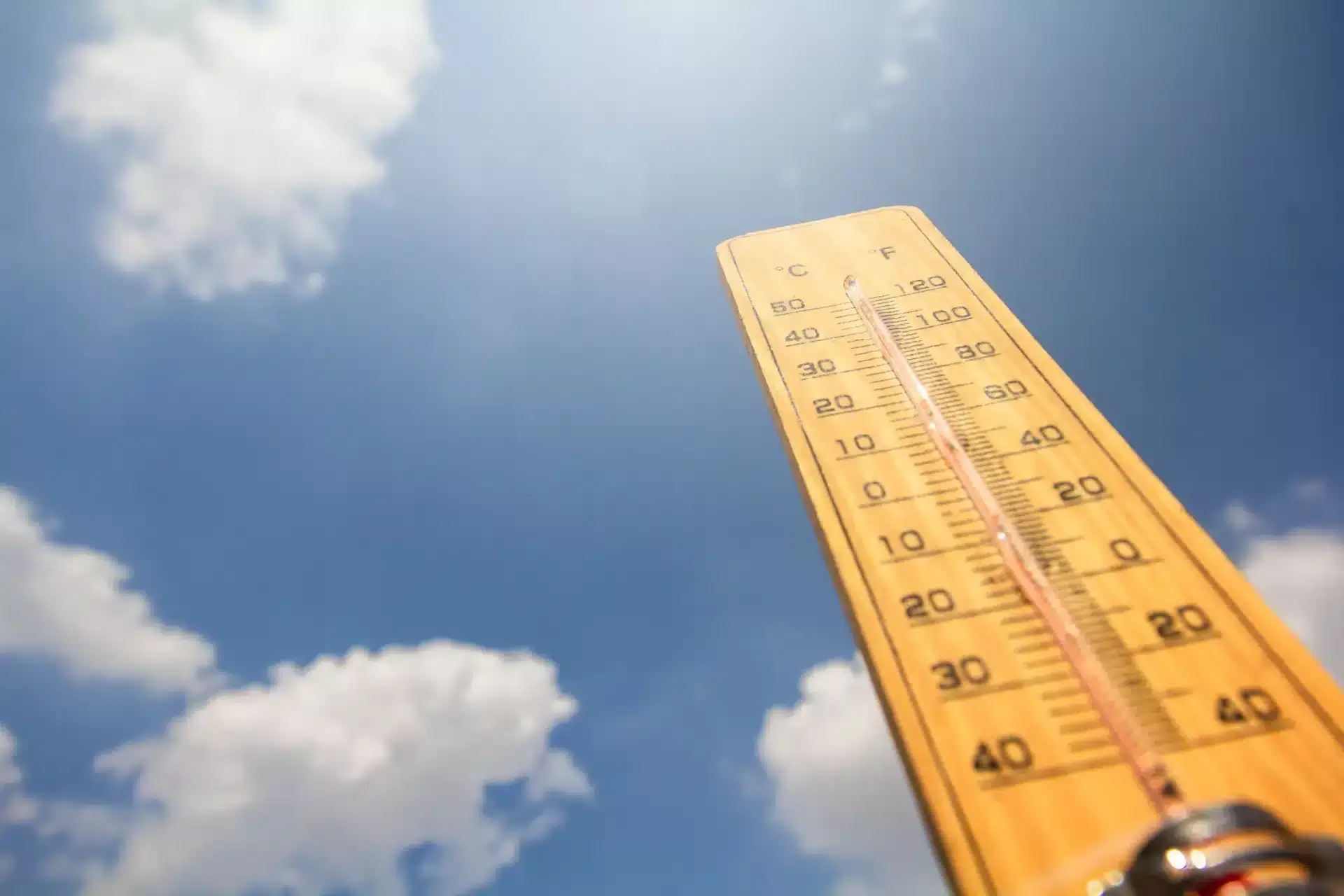 A thermometer pointing up into a lightly clouded blue sky.